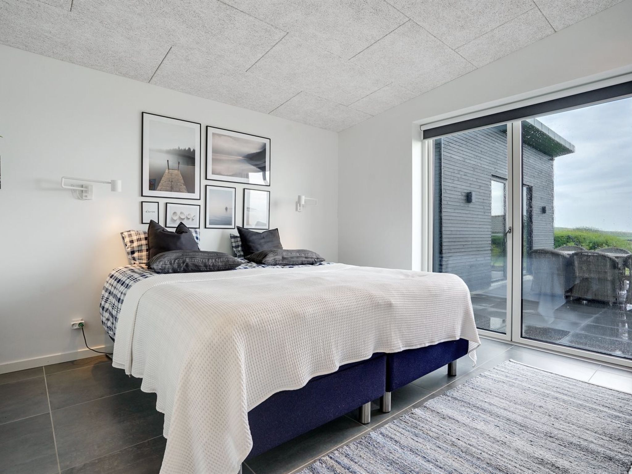 A modern bedroom with a large bed, a view of the outdoors, and a ceiling with recessed lighting.
