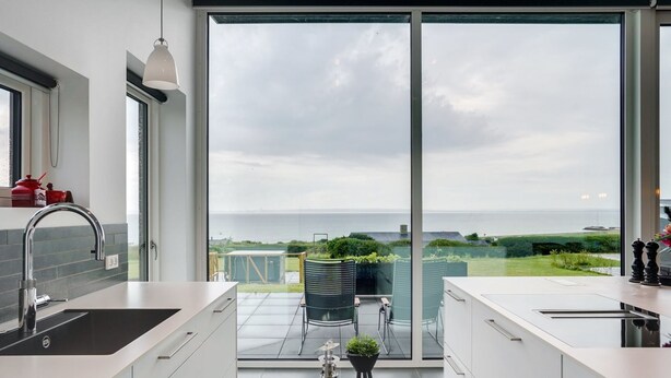 Une cuisine moderne dot ée d’une grande porte-fenêtre coulissante qui donne sur un balcon offrant une vue sur la mer.
