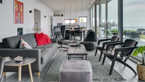 Un salon moderne avec un canapé gris, des fauteuils noirs, une table basse et une grande fenêtre donnant sur la ville.