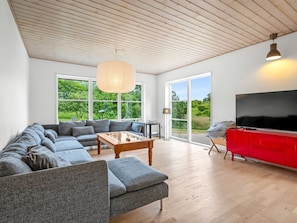 En moderne stue med en modulsofa, et sofabord, et rødt tv-møbel og et stort fjernsyn.