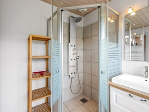 Un baño con ducha, lavamanos, espejo y estante de madera.