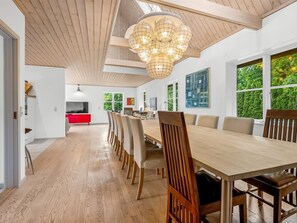 Un comedor moderno con una larga mesa de madera, varias sillas, un armario rojo y un amplio ventanal con vistas a zonas verdes.
