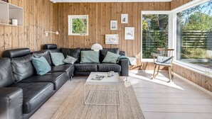 Ett modernt vardagsrum med en svart lädersoffa, ett soffbord och ett stort fönster med utsikt över omgivningen.