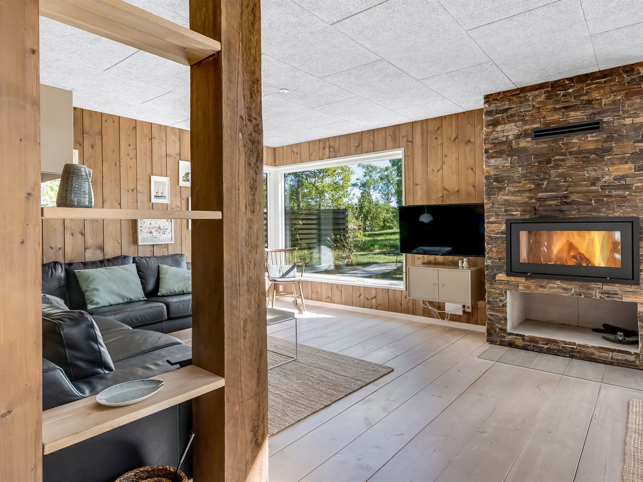 Ein modernes Wohnzimmer mit Kamin, Holzwandverkleidung, einem schwarzen Ledersofa und einem Fernseher.