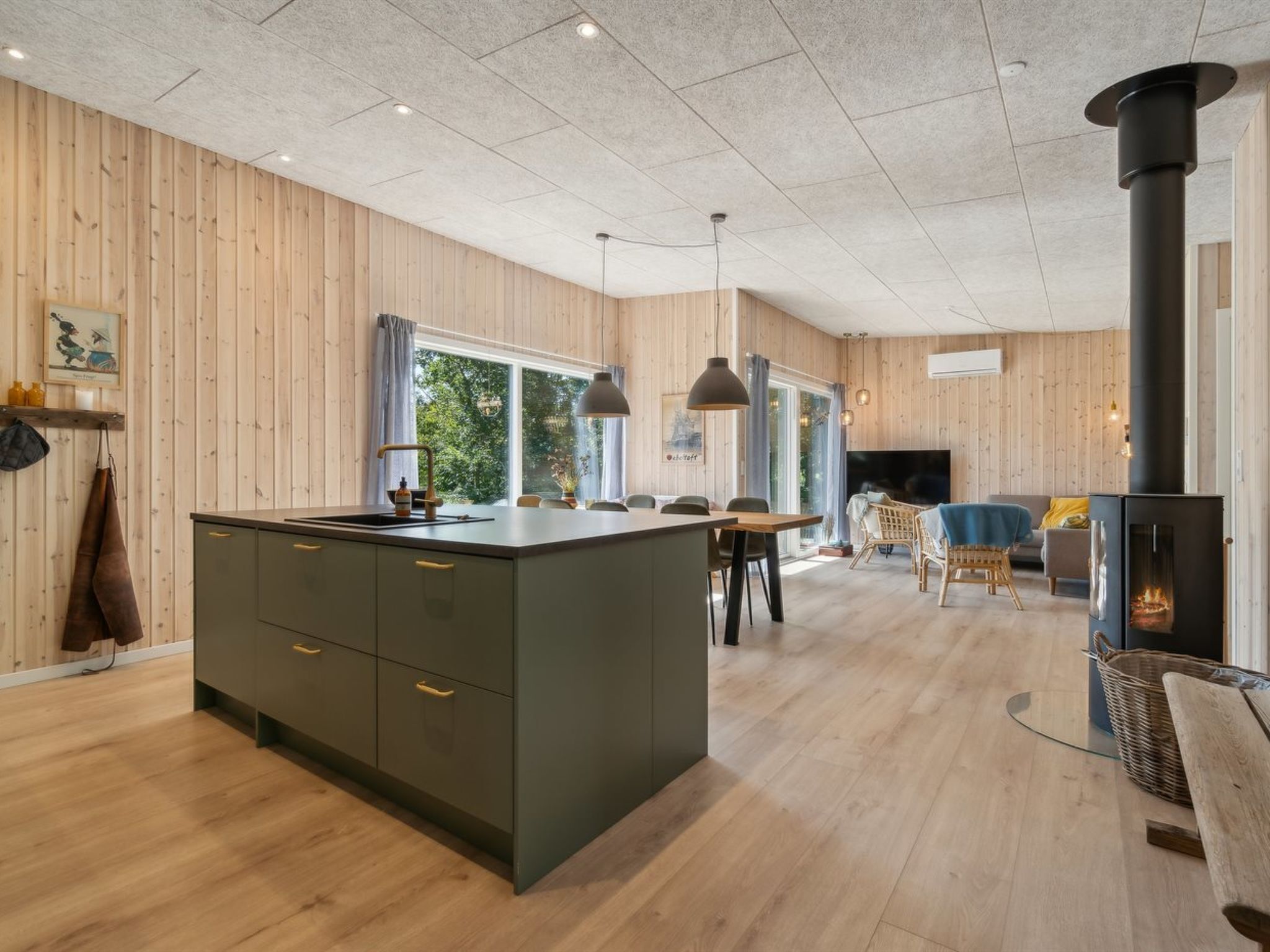 A modern kitchen with a central island, wooden walls, and a large window providing natural light.