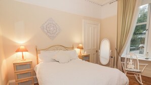 Une chambre à coucher avec un grand lit, deux tables de chevet avec des lampes, une commode, un miroir et une fenêtre avec des rideaux.