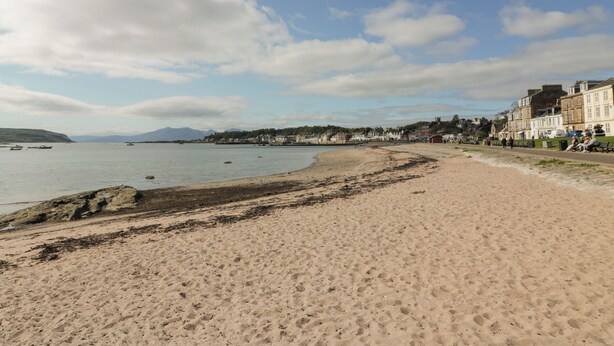 Une plage de sable fin, une mer calme, des bâtiments le long de la côte et un ciel dégagé.