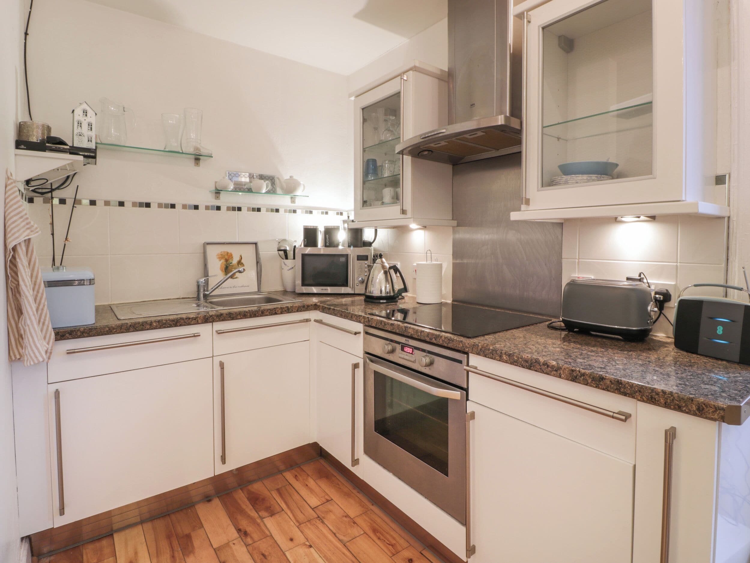 A modern kitchen with white cabinets, a granite countertop, stainless steel appliances, and wooden flooring.