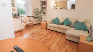 Un salon avec un canapé beige, une table basse en bois et une petite table d’appoint. On y trouve également un fauteuil, une bibliothèque et une plante en pot.