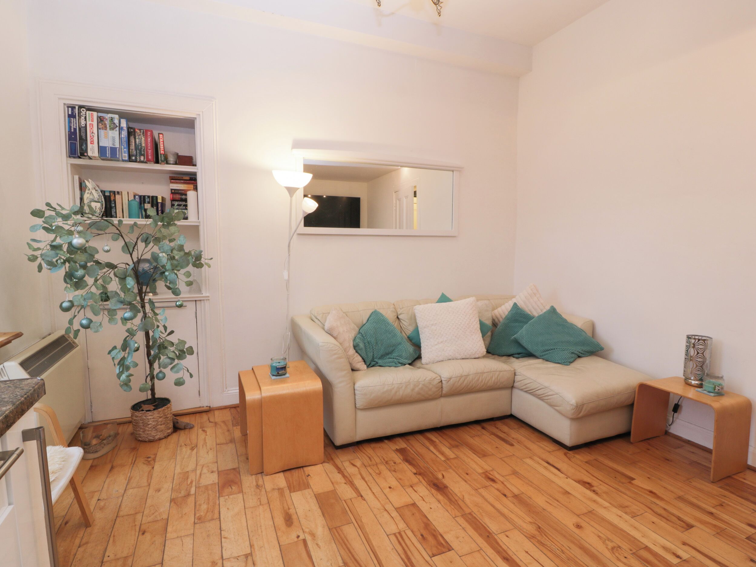 Una sala de estar con un sofá color beige, una mesita de madera, una lámpara de pie y una estantería llena de libros.