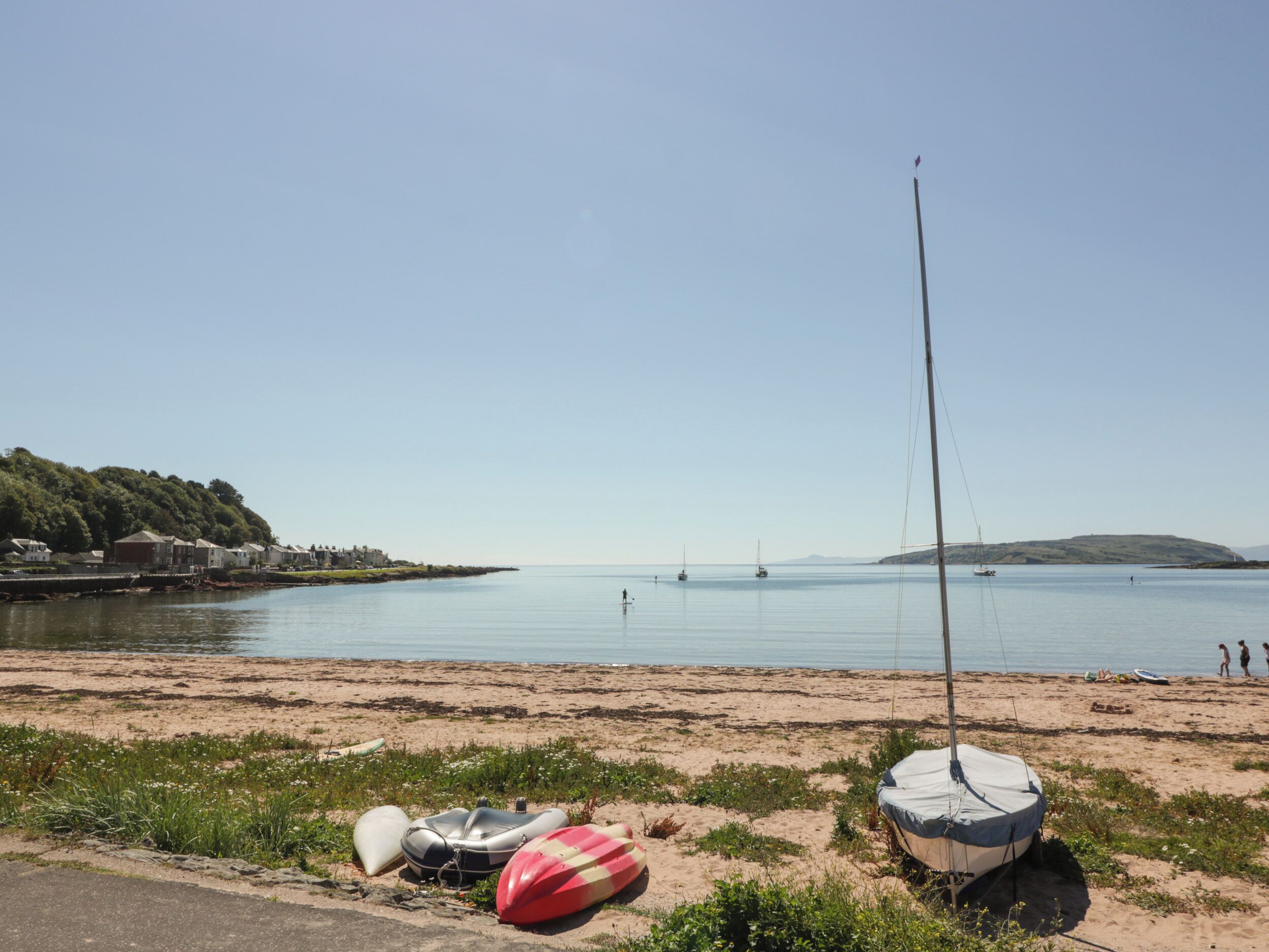 En strand med række af huse på en bakke, et roligt hav og flere både.