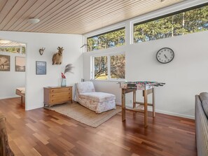 Une pièce avec un plancher en bois, un canapé, une petite table avec un jeu de baby-foot, une horloge et des tableaux encadrés au mur.