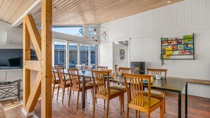 A dining area with wooden chairs and a table, a bookshelf with books, and a large window with a view.