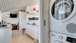 A compact kitchen with white cabinetry, a built-in oven, and a red stool.