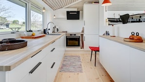 Een moderne keuken met witte kastjes, een houten aanrecht, een ingebouwde oven en een rode stoel.