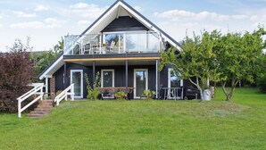Een modern huis met twee verdiepingen, een balkon, een overdekte zithoek en een verzorgd gazon.