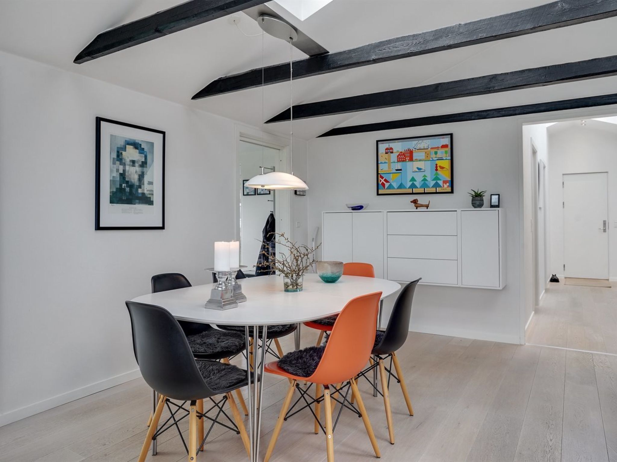 Un espace repas moderne avec une table ronde, des chaises noires et orange, et un plafond blanc avec des poutres apparentes.