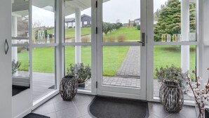Ein Wintergarten mit großen Glasüren, Fliesenboden und zwei Korbstühlen.
