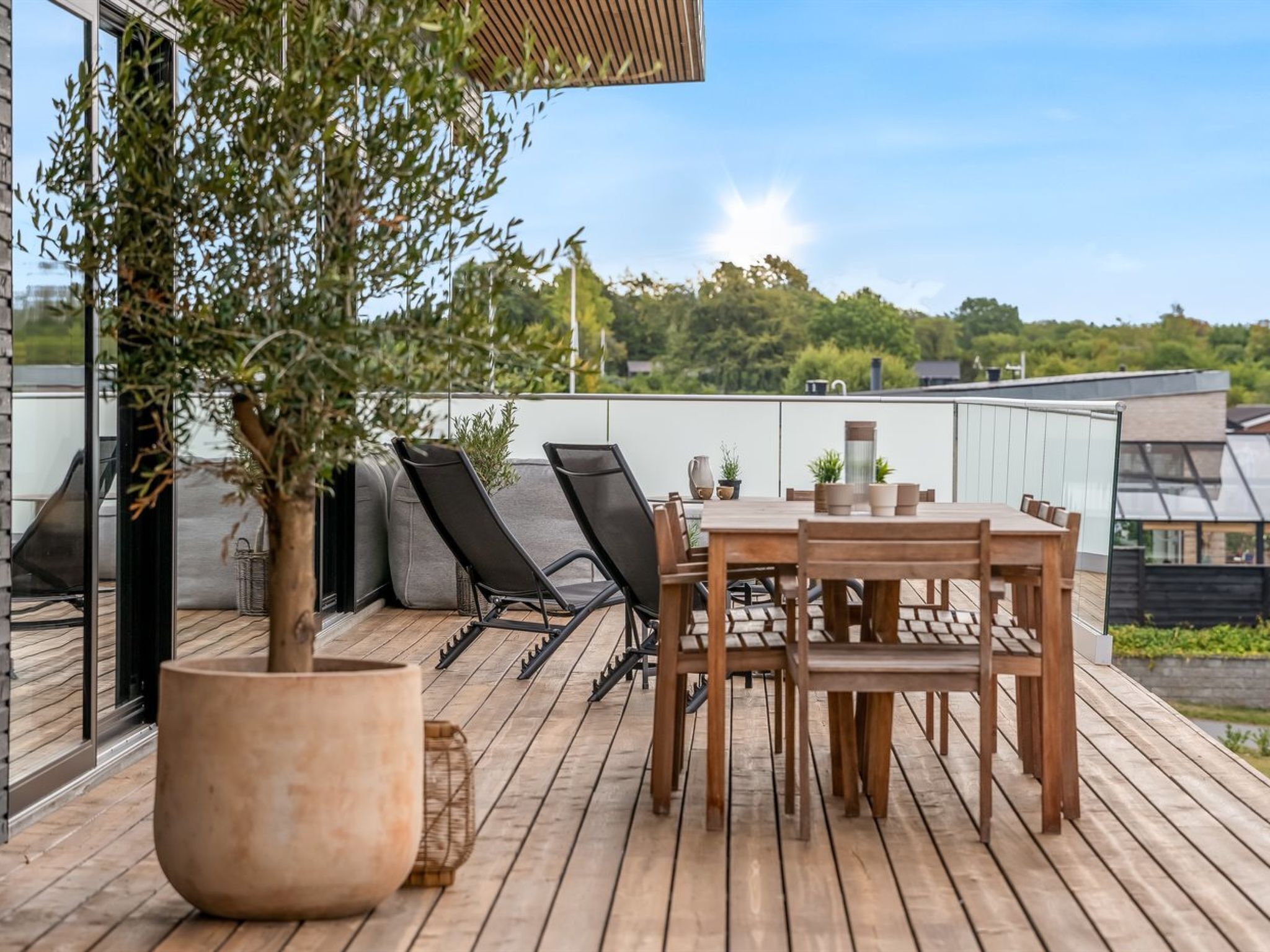 A wooden deck with a table and chairs, a large potted plant, and a view of the surrounding area.