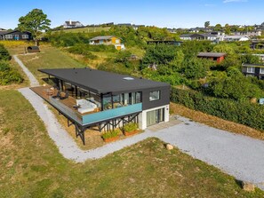 Une maison moderne dotée d’une terrasse, de grandes fenêtres et offrant une vue sur un quartier situé sur une colline.