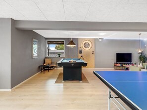 Une pièce équipée d’une table de billard, d’un jeu de fléchettes, d’un téléviseur et d’un coin salon avec une chaise et une table.