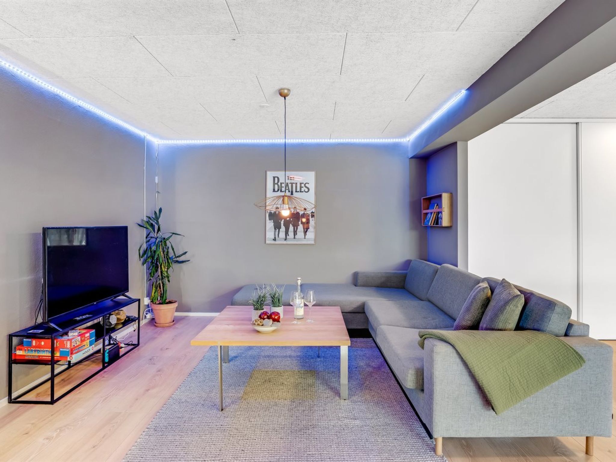 Un salon moderne avec un téléviseur à écran plat, une table basse, un canapé et une affiche accrochée au mur.