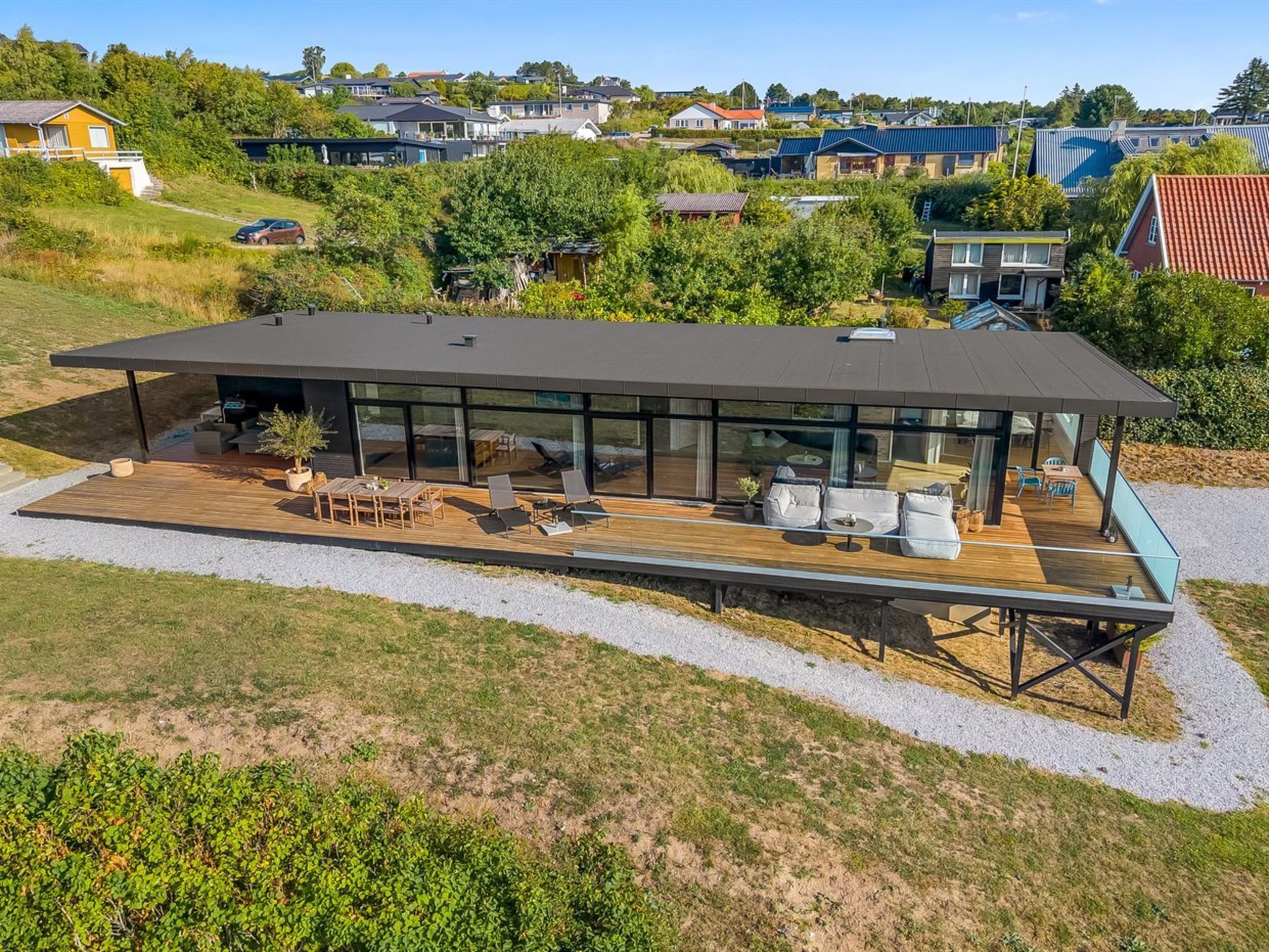 A modern house with a large deck, outdoor furniture, and a view of the surrounding neighborhood.