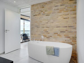 A modern bathroom with a large bathtub, a brick wall, and a view of the outdoors.
