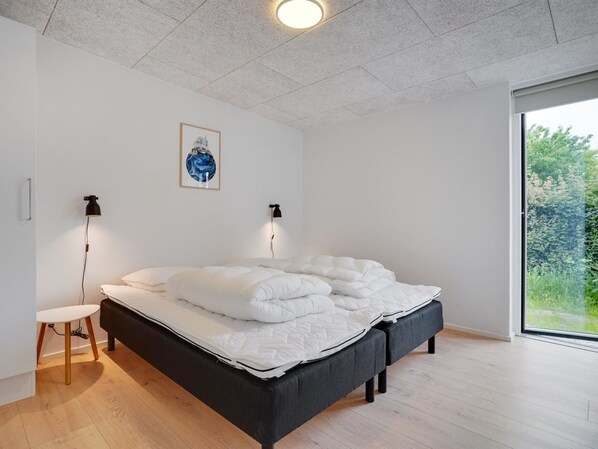 A modern bedroom with a bed, bedside lamps, a small table, and a large window offering a view of greenery. - "Ahmik" - 200m from the sea by Interhome (Ebeltoft)