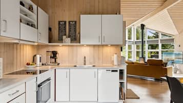 Une cuisine moderne avec des meubles blancs, une machine à café et une grande fenêtre donnant sur un paysage magnifique.