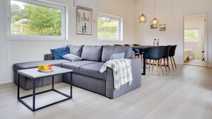 A modern living room with a grey sofa, a small table, and a dining area with chairs and a table.