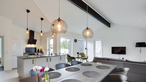 A modern kitchen with a central island, pendant lights, and a dining area with a long table and chairs.