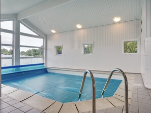 Una piscina interior con agua azul cristalina, escaleras de metal y vistas a la vegetación exterior.