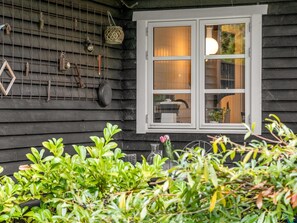 A wooden house with a white-framed window, a hanging light fixture, and various items like a lantern and a metal frame on the wall.