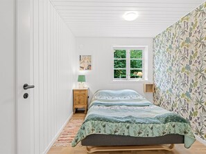 Un dormitorio con cama, mesita de noche, lámpara, ventana y puerta.