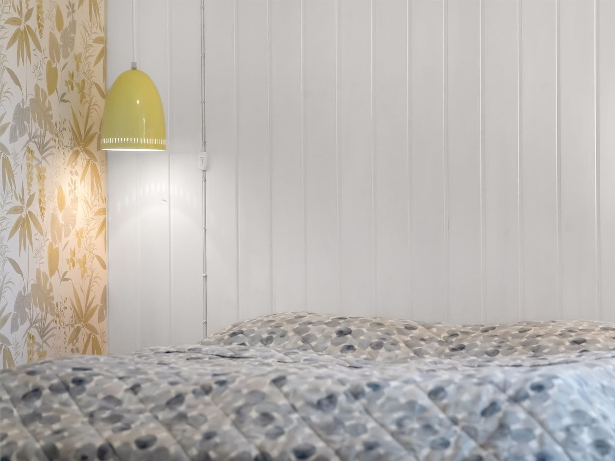 Un dormitorio con una colcha estampada, una lámpara de pared y un papel tapiz floral en una pared.