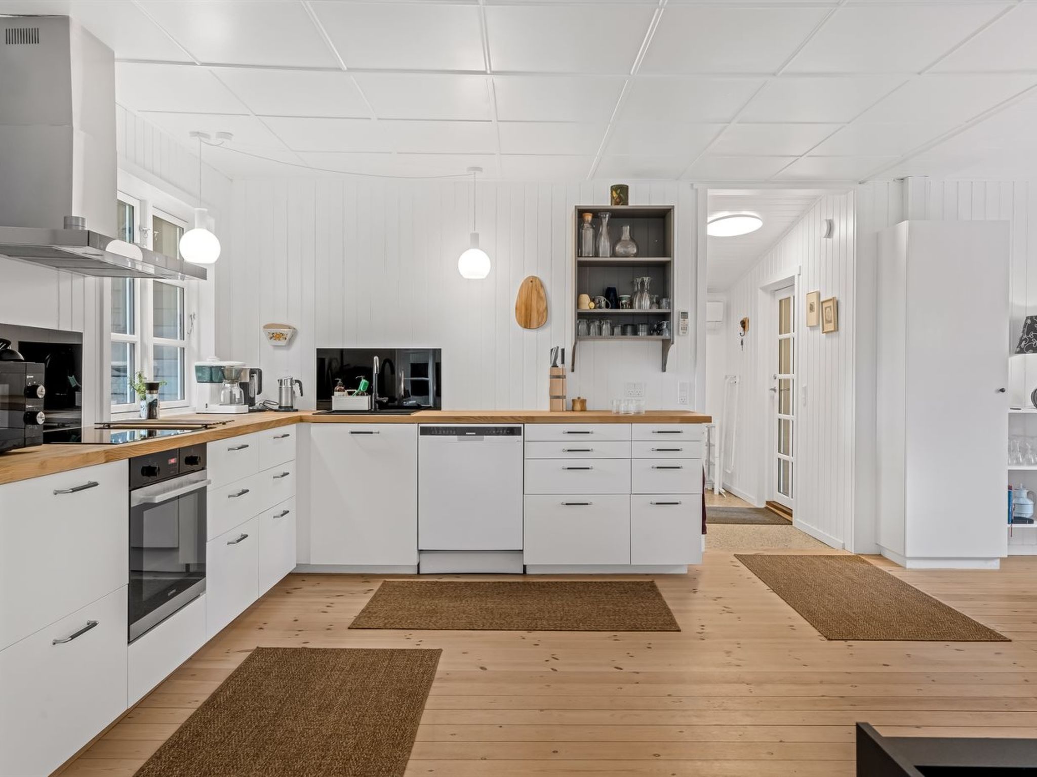 A modern kitchen with white cabinetry, wooden countertops, and a central island with a dishwasher.