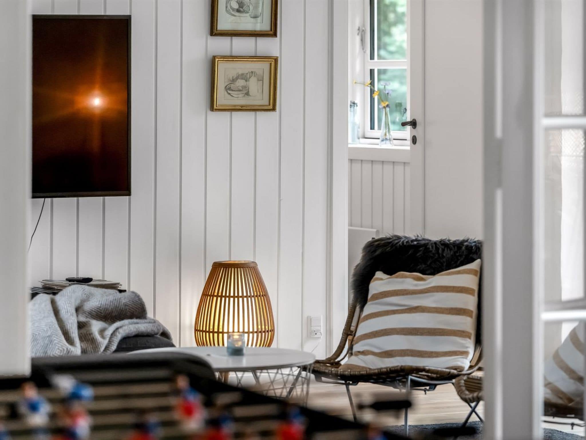 A modern living room with a television, framed artwork, a lamp, and a chair with a striped pillow.