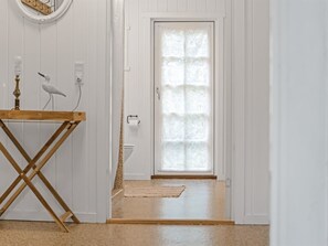 Um corredor com uma porta branca, uma mesa de madeira com abajur e uma escultura de pássaro.