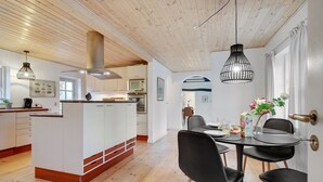 A modern kitchen with white cabinets, a central island, and a dining area with black chairs and a round table. - "Malinda" - 500m from the sea by Interhome (Odder)
