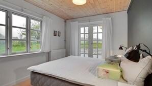 A bedroom with a bed, a bedside lamp, a radiator, and a window with curtains. - "Malinda" - 500m from the sea by Interhome (Odder)