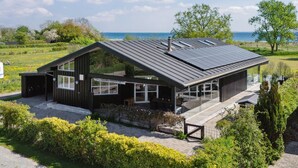 Ett modernt hus med ett sluttande tak, stora fönster och utsikt över havet.