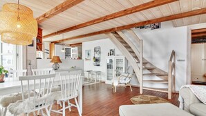 A spacious living area with wooden floors, white furniture, a staircase, and a dining area with a table and chairs.