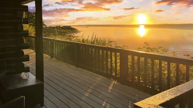A wooden deck with a railing overlooking a body of water during sunset.