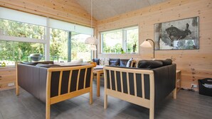 Une chambre confortable, aménagée dans le style d’un chalet, avec un intérieur en bois, un canapé, une table à manger et de grandes fenêtres donnant sur l’extérieur.