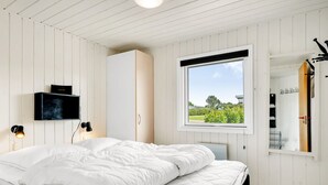 Une chambre à coucher comprenant un lit, une armoire, un téléviseur et une fenêtre donnant sur un paysage verdoyant.