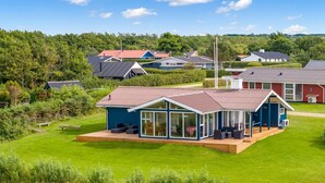 Une maison moderne dotée d’une grande terrasse, entourée d’une végétation luxuriante et d’autres maisons.