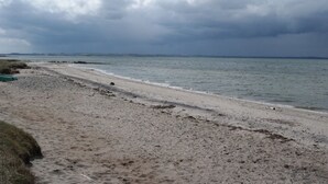 Une plage avec un rivage sablonneux et une vue sur la mer, sous un ciel nuageux.