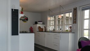 Une cuisine moderne avec des meubles blancs, un tableau noir sur lequel est écrit un message de bienvenue, des luminaires suspendus et une vue dégagée grâce à de grandes fenêtres.