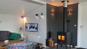 Un salon moderne avec une cheminée, un téléviseur fixé au mur et un canapé recouvert d’un tissu aux couleurs vives.